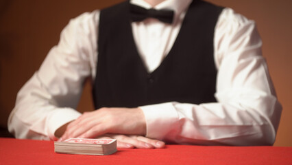 Casino dealer shuffles cards on red table, hands close up.