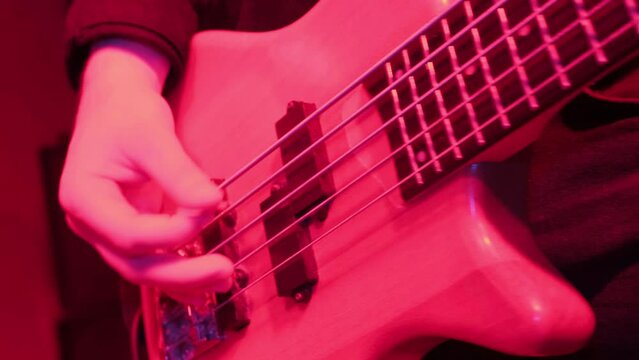Hands of rock musician playing the electric bass guitar on repetitin in red light.