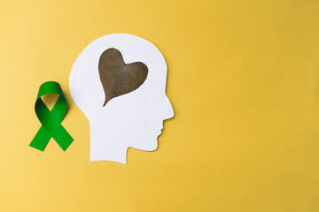 green ribbon, head silhouette with heart on yellow background. world mental health day concept. Copy space.