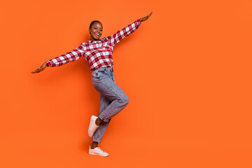 Full body photo of cheerful pretty person raise hands flight have good mood isolated on orange color background