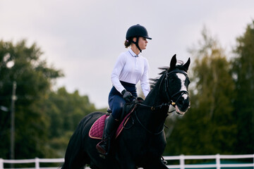 Sports training. Young sportive girl, professional rider in sports uniform and helmet practicing at...