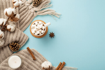 Fototapeta na wymiar Top view photo of knitted plaid cup of hot drinking with marshmallow on rattan serving mat cotton branch candle pine cones cinnamon sticks and anise on isolated pastel blue background with copyspace