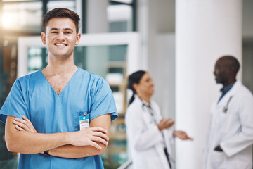 Portrait of a male nurse with his team in the background in the hospital. Happy, smiling and confident nurse with doctors in medicine, health and medical care. Medical team, healthcare and nursing - obrazy, fototapety, plakaty