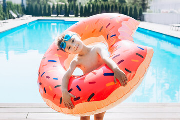 Funny little boy in a swimming pool with donat life preserver