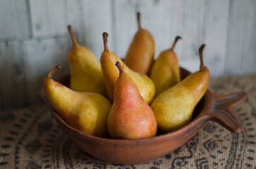 Juicy ripe pears in a clay bowl on a hemp tablecloth with an ornament.
