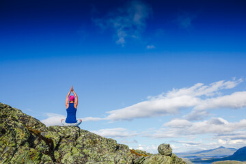 Young woman is practicing yoga high in the mountains