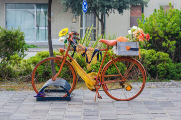 Una bicicletta colorata di arancione e decorata con dei fiori e una cassetta di legno con un cuore parcheggiata in una rastrelliera
