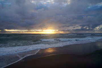 dark clouds of a storm under which sunbeams of the sunset shine on the sea seen from the beach, North Sea