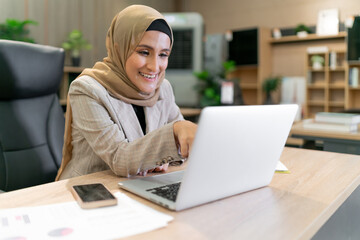 happy business muslim hijab woman work. islam woman pointing at laptop screen while having an online group meeting. success cheerful adult beautiful arabic person sitting touch screen consult people