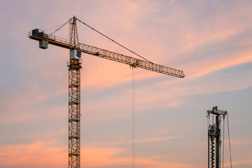 Construction equipment against sunset sky. Red tower crane