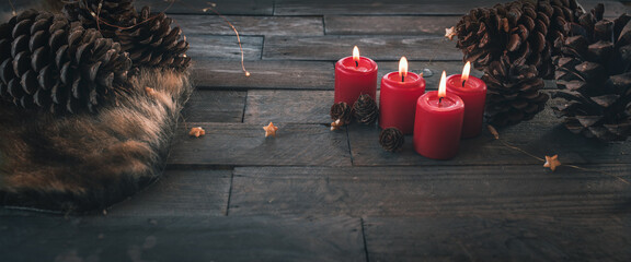 Four burning red christmas candles, dekorated on dark wood with fairy lights and pine cone....