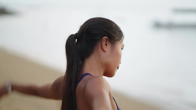 Close up of young pretty asian woman warm up on beach at sunrise before workout in Bali Indonesia. Ocean in background