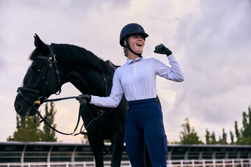 Winner. Young sportive girl, professional jockey or horsewoman in sports uniform and helmet with...