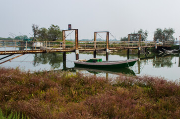 Obraz premium Una barca bianca e verde ormeggiata vicino a un pontile in un canale delle Valli di Comacchio in una giornata nuvolosa