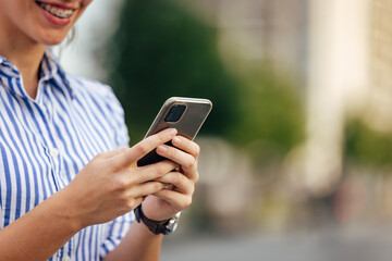 Close up of a smiling girl holding and using a mobile phone.