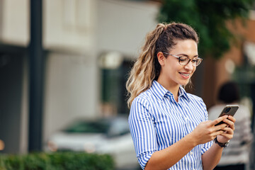 Blonde girl being outdoor, using a mobile phone, chatting with someone.