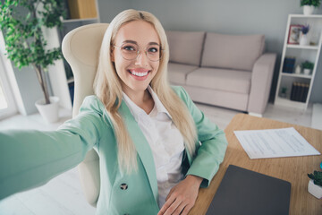 Portrait of charming cheerful person sitting chair make selfie record video showing workplace...