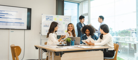 Young and successful mixed race, asian business people working on project together, sitting at...