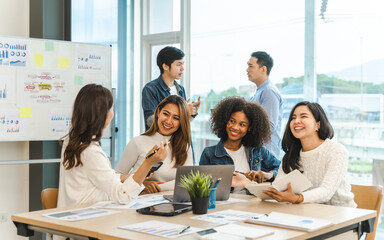Young and successful mixed race, asian business people working on project together, sitting at...