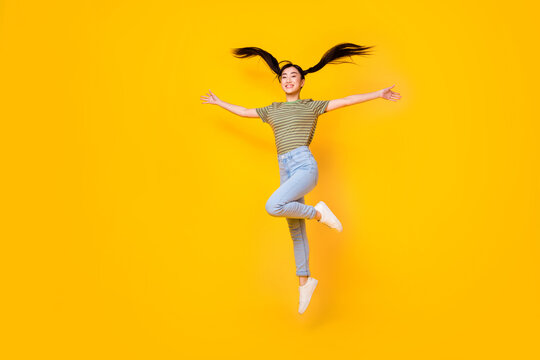 Full length picture of energetic young lady jumping up flying hair two ponytails hairstyle isolated on yellow color background