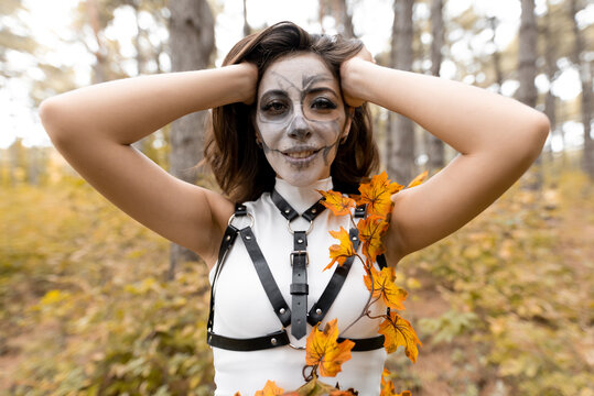 Halloween portrait of a young beautiful girl in a white dress with makeup on her face. Posing in the autumn forest. Skeleton face makeup. The day of the Dead