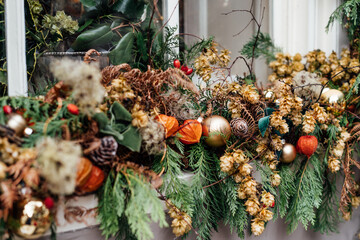 Close up winter holiday window decorated with fresh greens, red berries, cones and flowers. Outdoor...