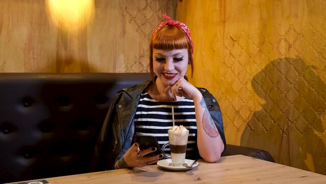 Tattooed redhead girl having a coffee and chatting on her phone