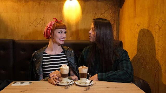 Young long-haired brunette guy talking to a tattooed red-haired girl in a coffee shop