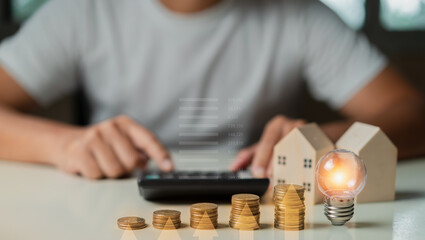 Man using calculator to calculate and Stacking coins, light bulb,wooden house on table. Saving money,accounting, investment, budgeting, and financial planning concept.
