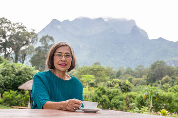 Asin senior woman drinking coffee in cafe outdoor with mountain view.