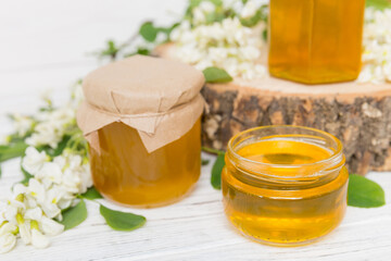 Sweet honey jar surrounded spring acacia blossoms. Honey flows from a spoon in a jar. jars of clear fresh acacia honey on wooden background