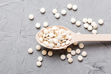 Heap of white pills on colored background. Tablets scattered on a table. Pile of red soft gelatin capsule. Vitamins and dietary supplements concept