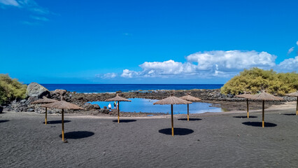 Fototapeta na wymiar Scenic sea view on beach Playa Charco del Conde without people in Valle Gran Rey, La Gomera, Canary Islands, Spain, Europe. Straw umbrellas in the dark volcanic sand. Vacation vibes in tropical bay
