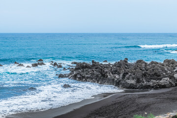 Black sand on the beach near the volcanic rocks in the Atlantic Ocean in the Canary Islands, Spain. Seascape of the coast of the Atlantic Ocean with waves for surfing on the surface of the water
