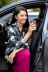 Obraz na płótnie Canvas Beautiful modern young woman with a cup of coffee in her car. The driver automobile. Vacation trip. Lifestyle