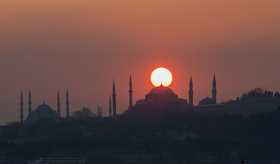 The view of the Blue Mosque and Hagia Sophia at sunset and after sunset was photographed with a tele zoom lens. - obrazy, fototapety, plakaty