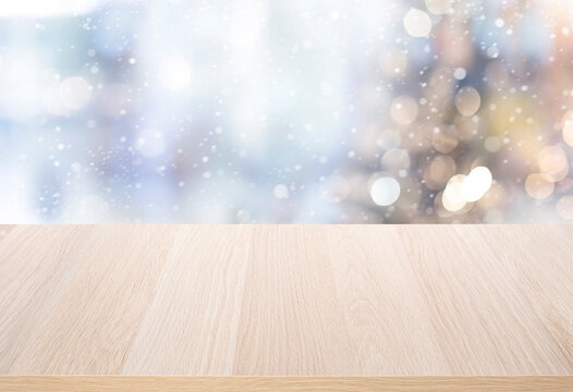 Selective focus.Empty wood table top with snowfall and blur of christmas tree in winter background.