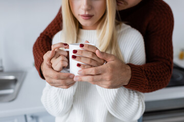 cropped view of young man hugging blonde woman with cup of tea.