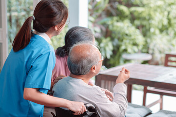 Fototapeta premium Asian caregiver nurse support senior elderly man on wheelchair in living room. nurse female take care of mature patient doing physical therapy at nursing home. Health care concept.