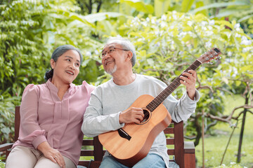Happy Asian senior couple elderly man playing guitar music song enjoy having fun happiness outside house near backyard garden. Retirement insurance concept