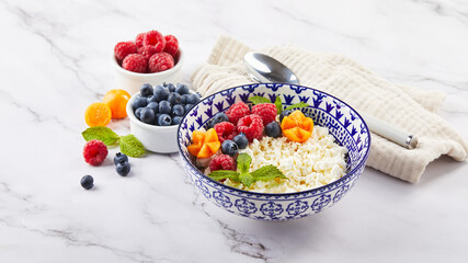 Cottage cheese in bowl garnished with raspberries, blueberries, physalis and mint leaves on white...