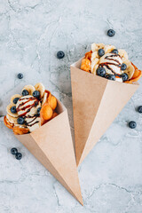 Bubble waffle with ice cream, banana and blueberry in paper cup over gray marble background