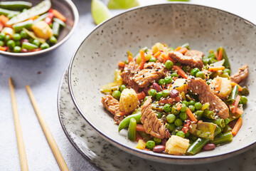 Wok with turkey meat, corn, green peas, green beans and carrots served on gray background with chopsticks. Asian food concept of street food
