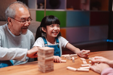 Asian happy family of little daughter play toy wooden block in home. Grandparents and young woman...