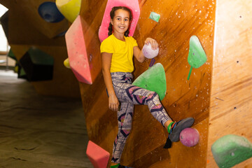 Cute little girl climbing on artificial boulders wall in gym