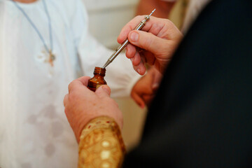 the priest holds the myrrh oil for the baptism of a boy in a baptismal shirt. 