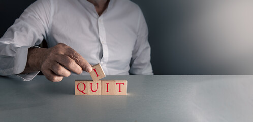 Man posing wooden blocks with I quit concept of leaving job resignation grey blue background with copy space .