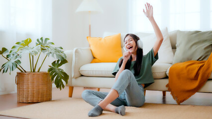 Young asian woman listening to music on on the floor beside couch in living room at home. Happy...