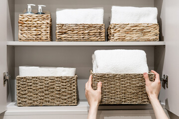 Woman is putting spare towels in bathroom closet