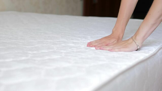 Close up of a girl's hand checks the rigidity of a new comfortable orthopedic white mattress for the bed. Female hand pressed on orthopedic surface. Girl tests elasticity softness orthopedic mattress.